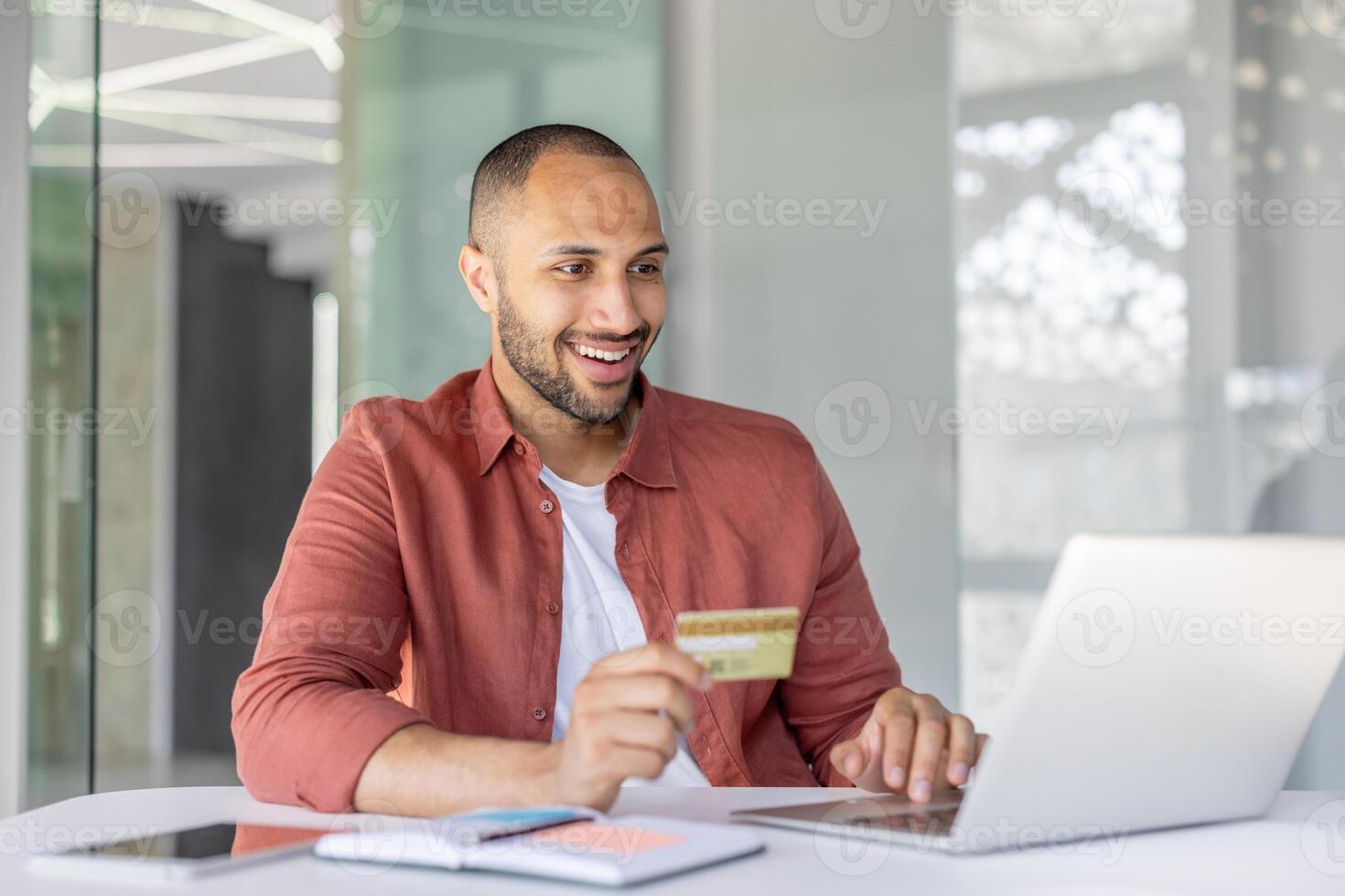 A happy man is shopping online and holding a credit card while seated at his computer photo