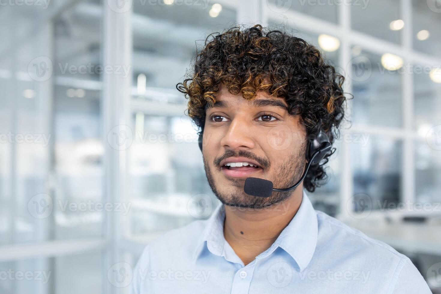 A young male customer service representative with a headset, engaging in conversation in a bright, modern office environment. Displays professionalism and approachability. photo