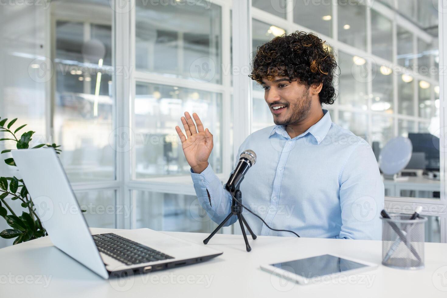 Cheerful young man in a light blue shirt engaging in a virtual business meeting or hosting a webinar from a well-lit office ,space with modern decor. photo