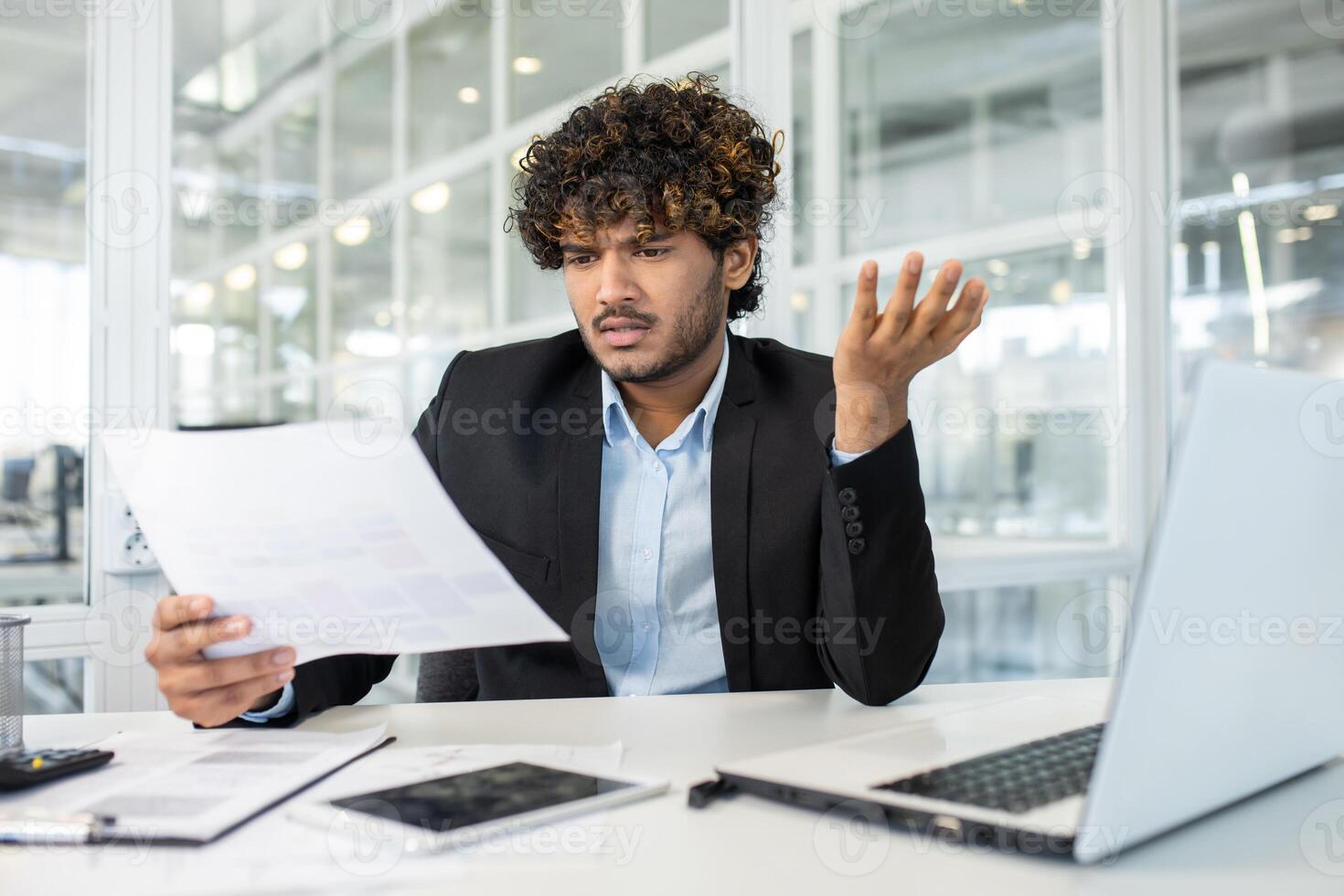 A young male entrepreneur expresses confusion and frustration while reviewing complex documents at his workplace, signaling challenges in business operations. photo