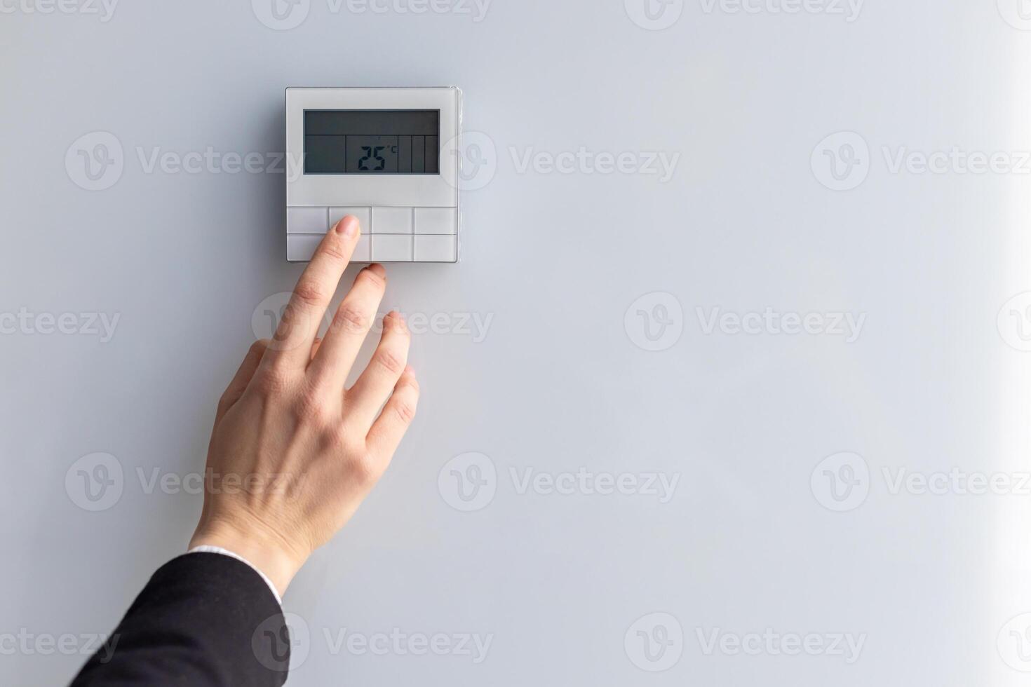 Close-up of hand adjusting digital thermostat set to 25 degrees Celsius. Concept of energy efficiency, climate control, and modern technology in home or office environment. photo