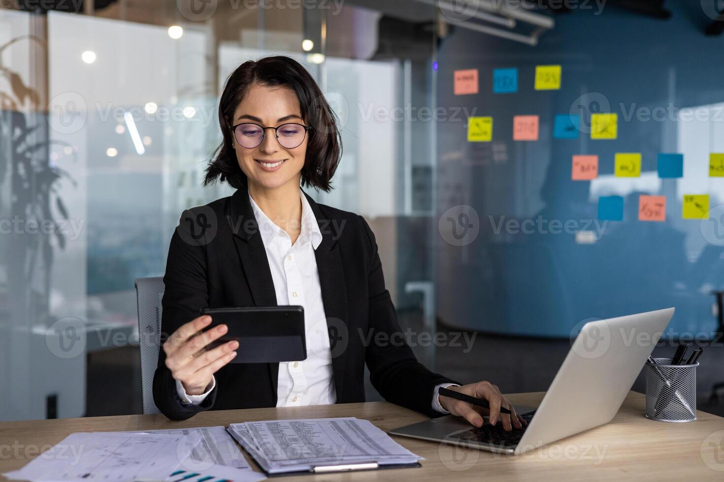 Confident businesswoman in modern office. Engaged in communication and multitasking with laptop and documents. Professional setting emphasizes success and productivity. photo