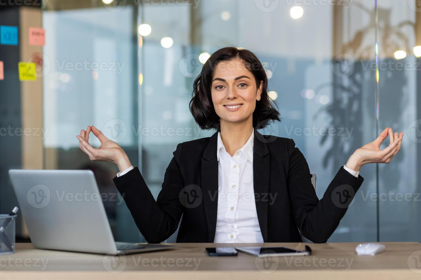 Confident woman in business suit practicing mindfulness yoga pose at office desk. Promotes calmness and focus during work. Ideal for themes related to meditation, stress management, and wellness. photo