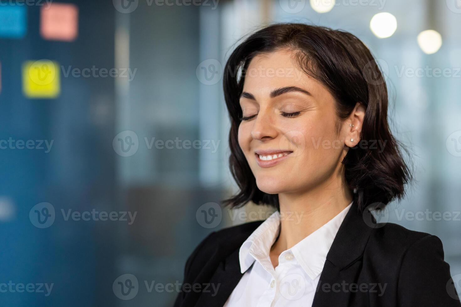 Confident professional woman in office setting practicing mindfulness with serene expression. Eyes closed, smiling softly, embracing peace, tranquility, stress relief, mental wellness. photo