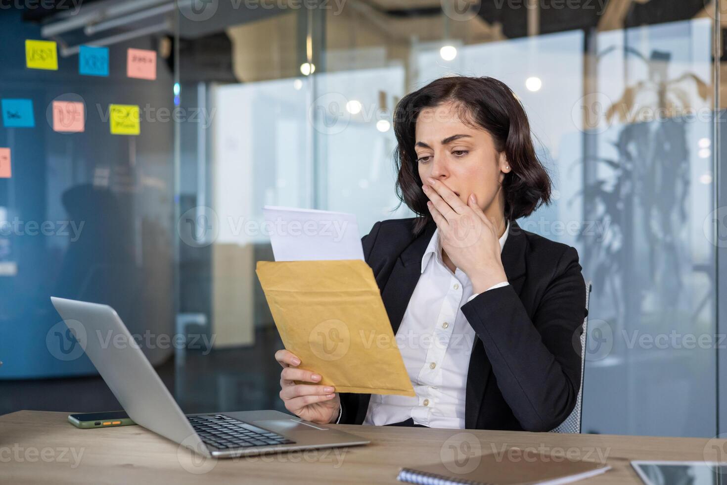 Businesswoman in modern office receiving important mail, expressing concern. Glancing at laptop, reflecting serious business communication or unexpected announcement. photo