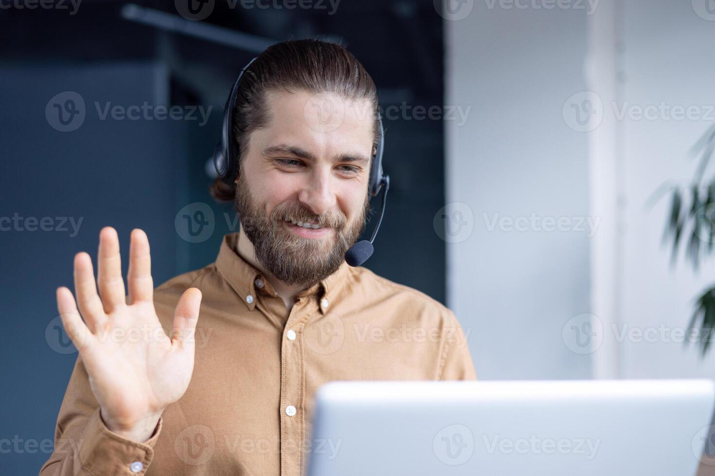 A man communicating in a call on a laptop, wearing a headset in a modern setting. photo