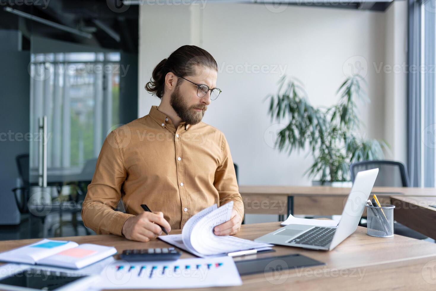A focused professional man is analyzing documents and charts in a contemporary office setup. photo
