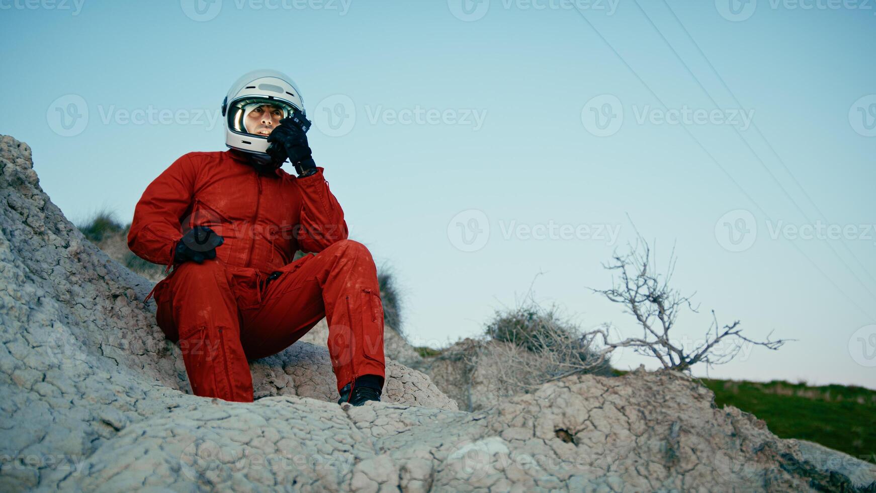 Astronaut With Orange Suit And Helmet Walks On The Rocks Of A Hostile Planet photo
