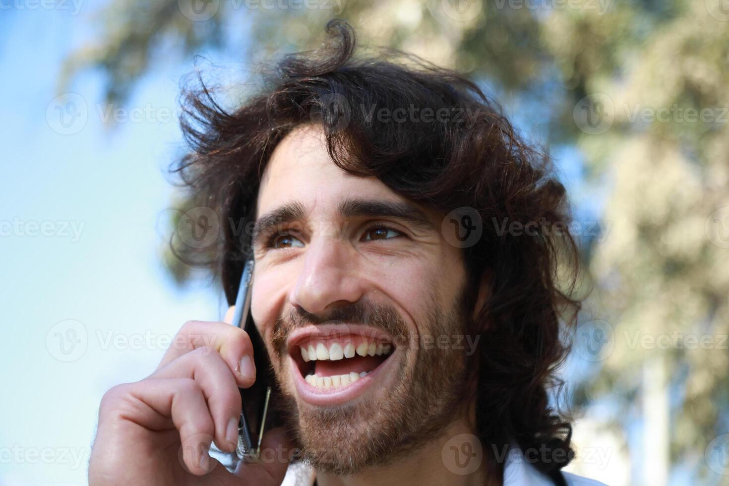 Long Hair Man Smiling Talking On The Phone Outside In The Park photo