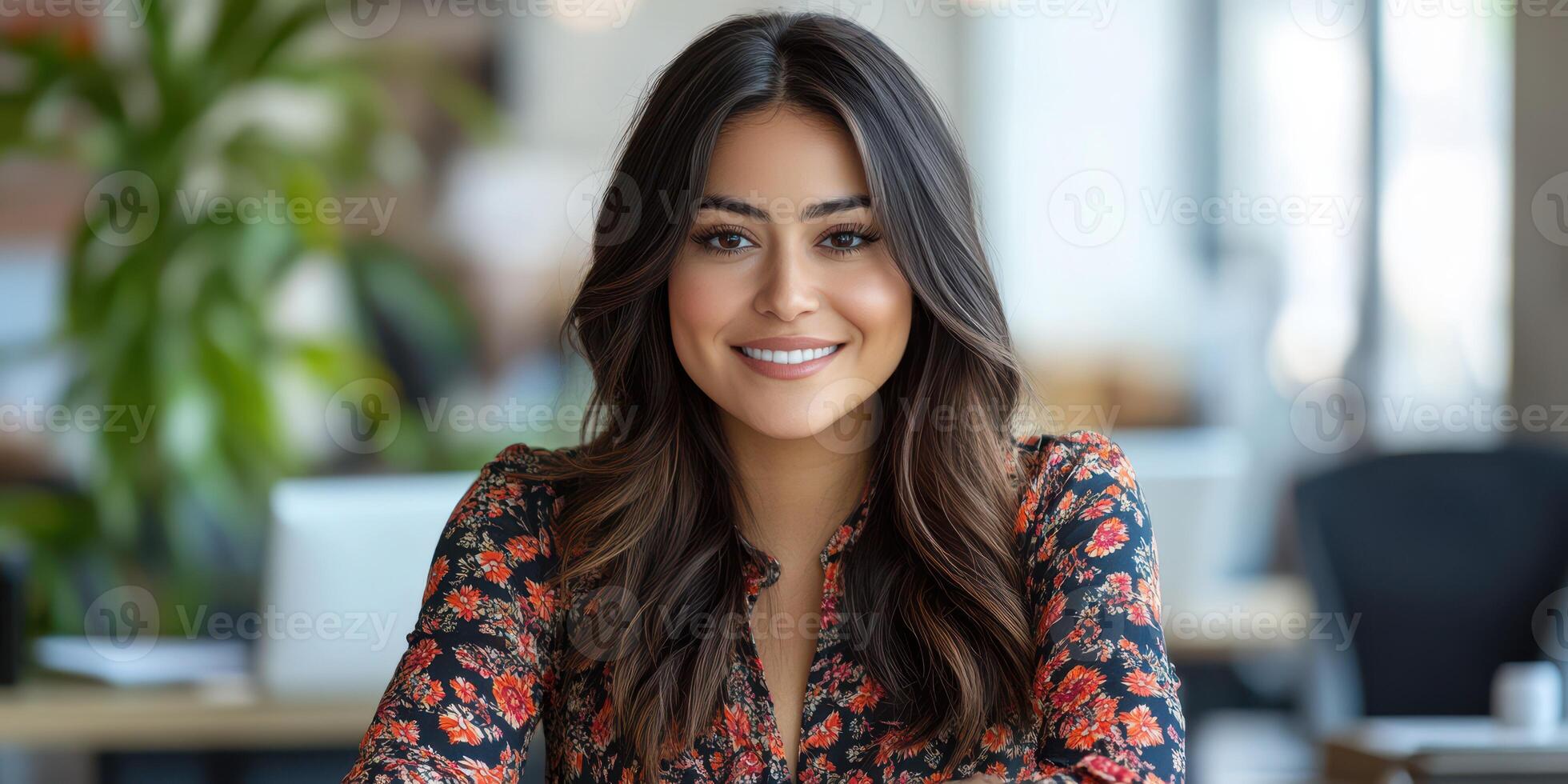 Smiling woman in floral dress sitting at desk in a modern office setting during daylight hours photo