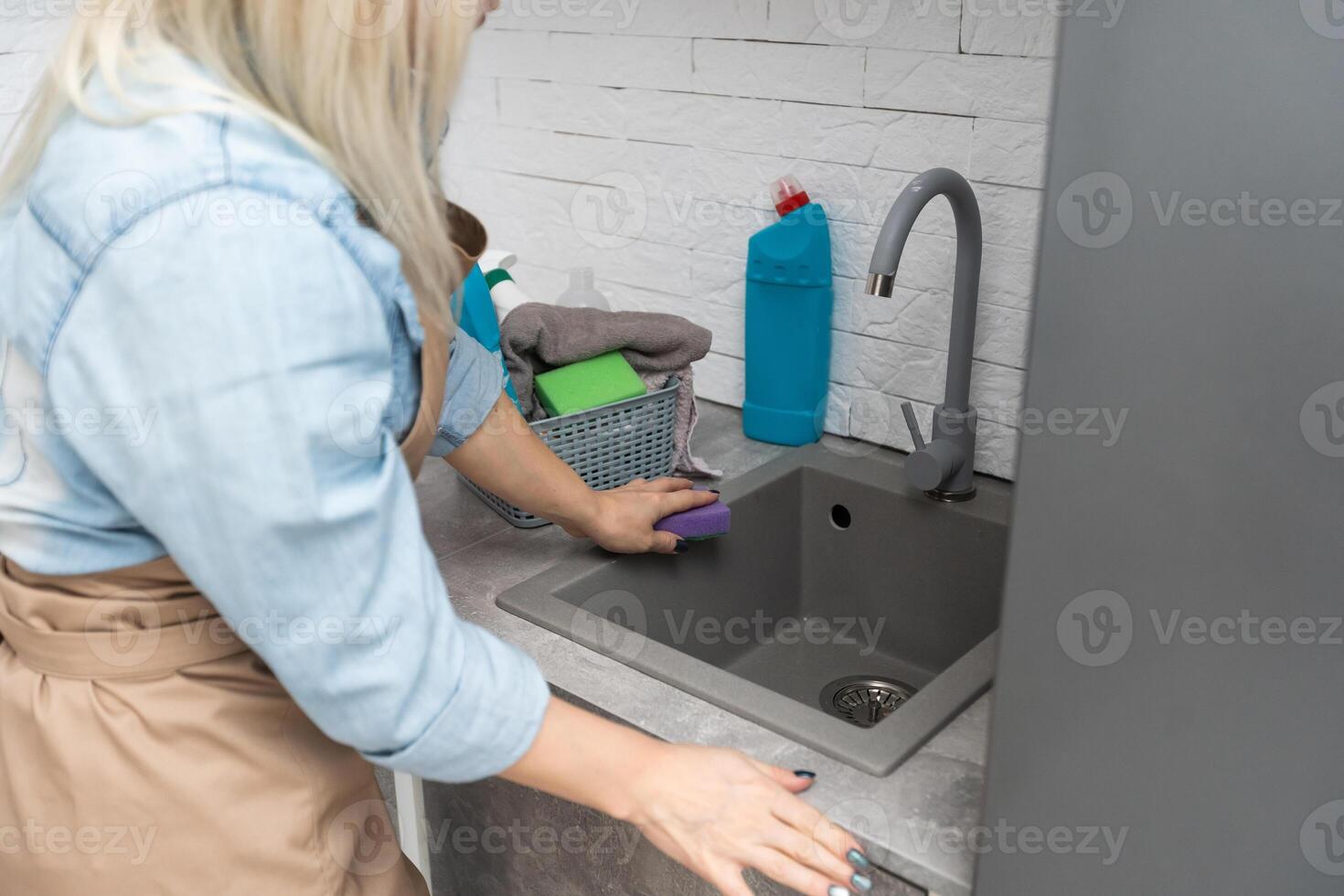 Cheerful Young Professional Cleaning Lady Wearing Apron Cleaning Stainless Steel Sink In Kitchen photo