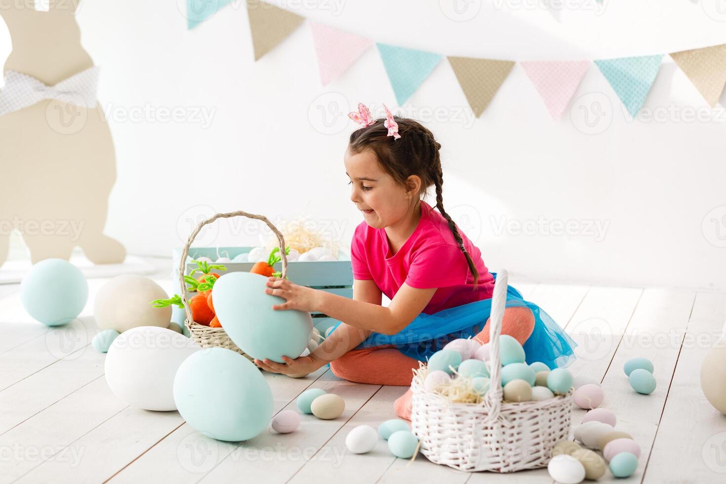 Getting ready to Easter. Lovely little girl holding an Easter egg and smiling with decoration in the background photo