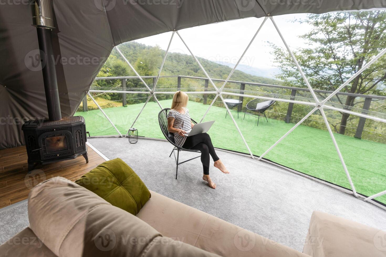 Young caucasian woman using and watching on laptop computer on in dome camping hotel. Tourism, vacation and weekend. photo