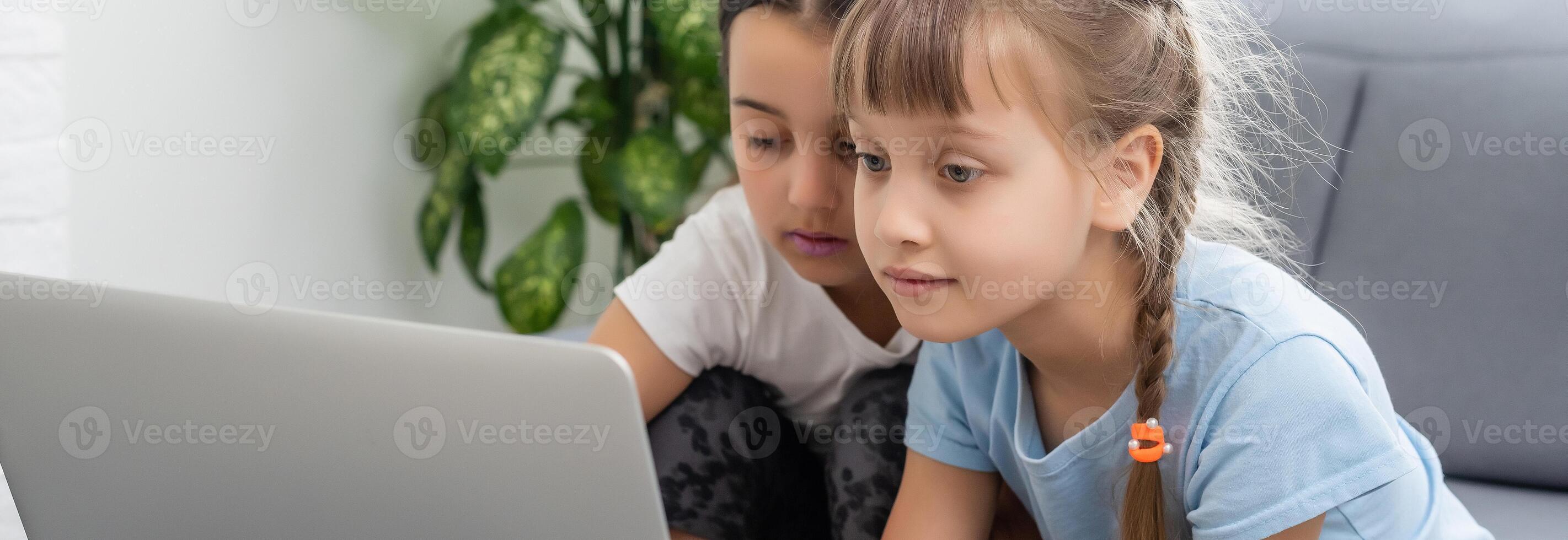 Little girls at home with laptop, chatting with their friends. photo