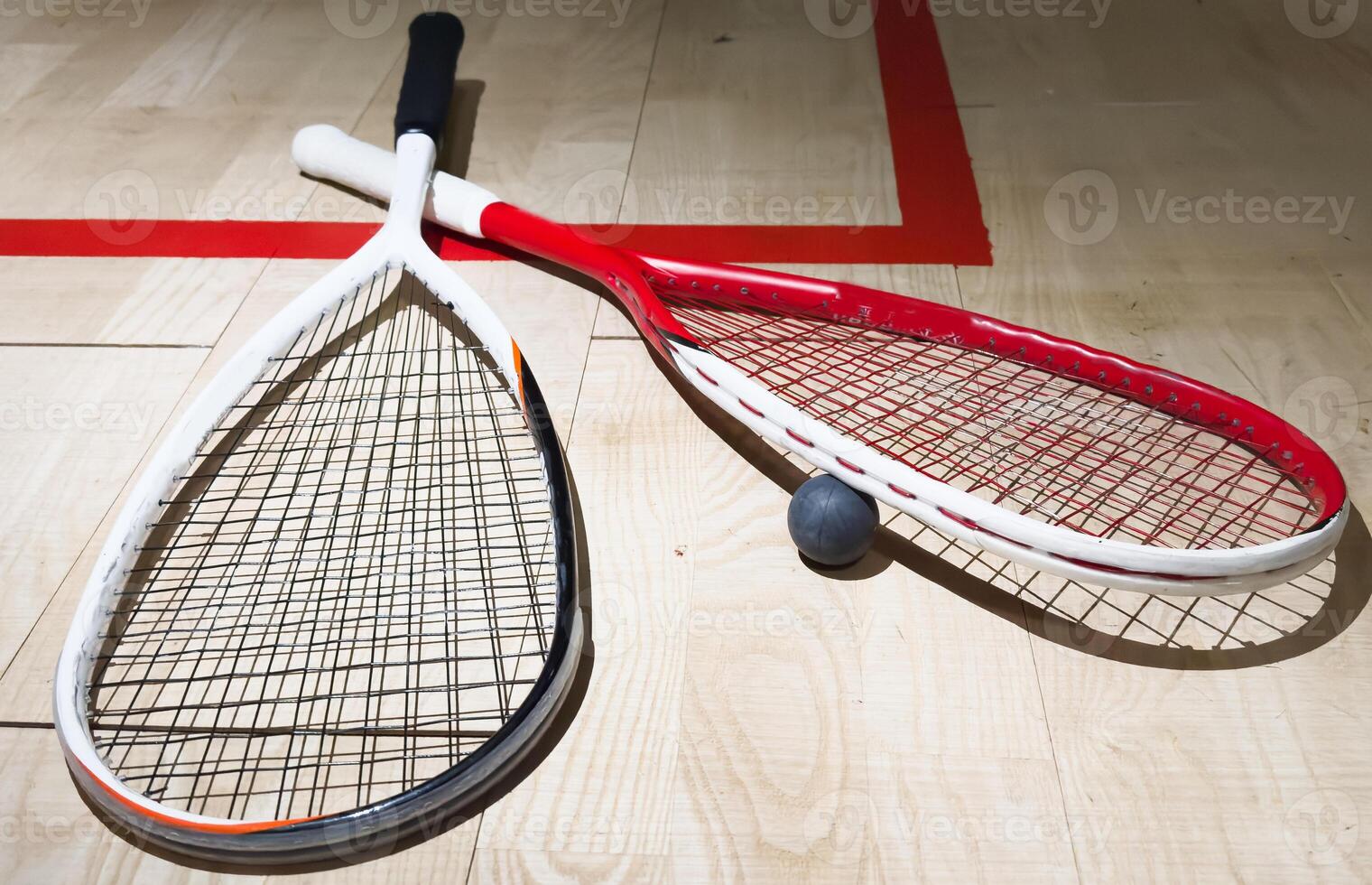 Two rackets and two squash balls lie on the parquet floor. Horizontal photo
