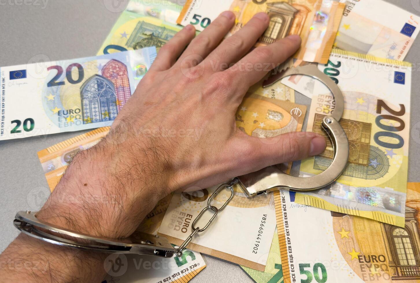 Folded hands and handcuffed hands resting on a table in front of money. photo