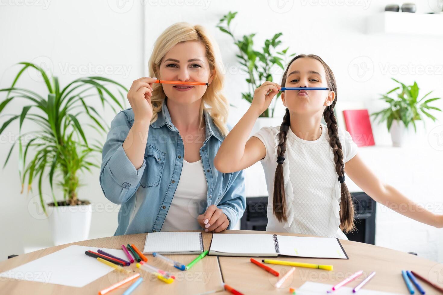 Mother and daughter beautiful and happy make a card for mother's day sitting together at the table with paper and pencils photo