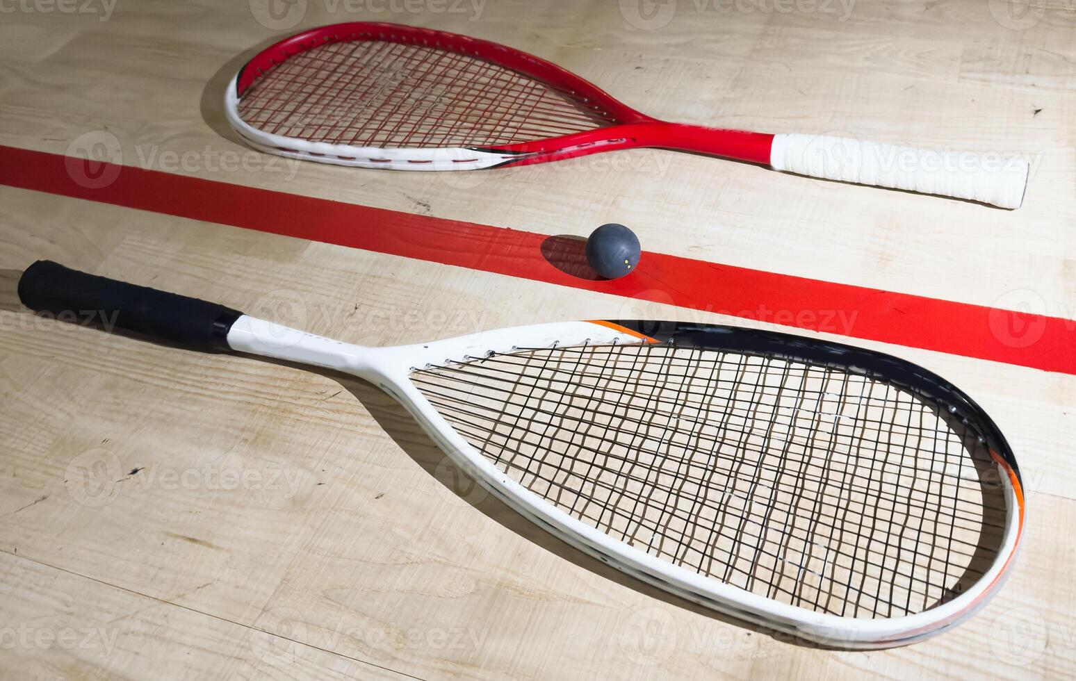 Two rackets and two squash balls lie on the parquet floor. Horizontal photo