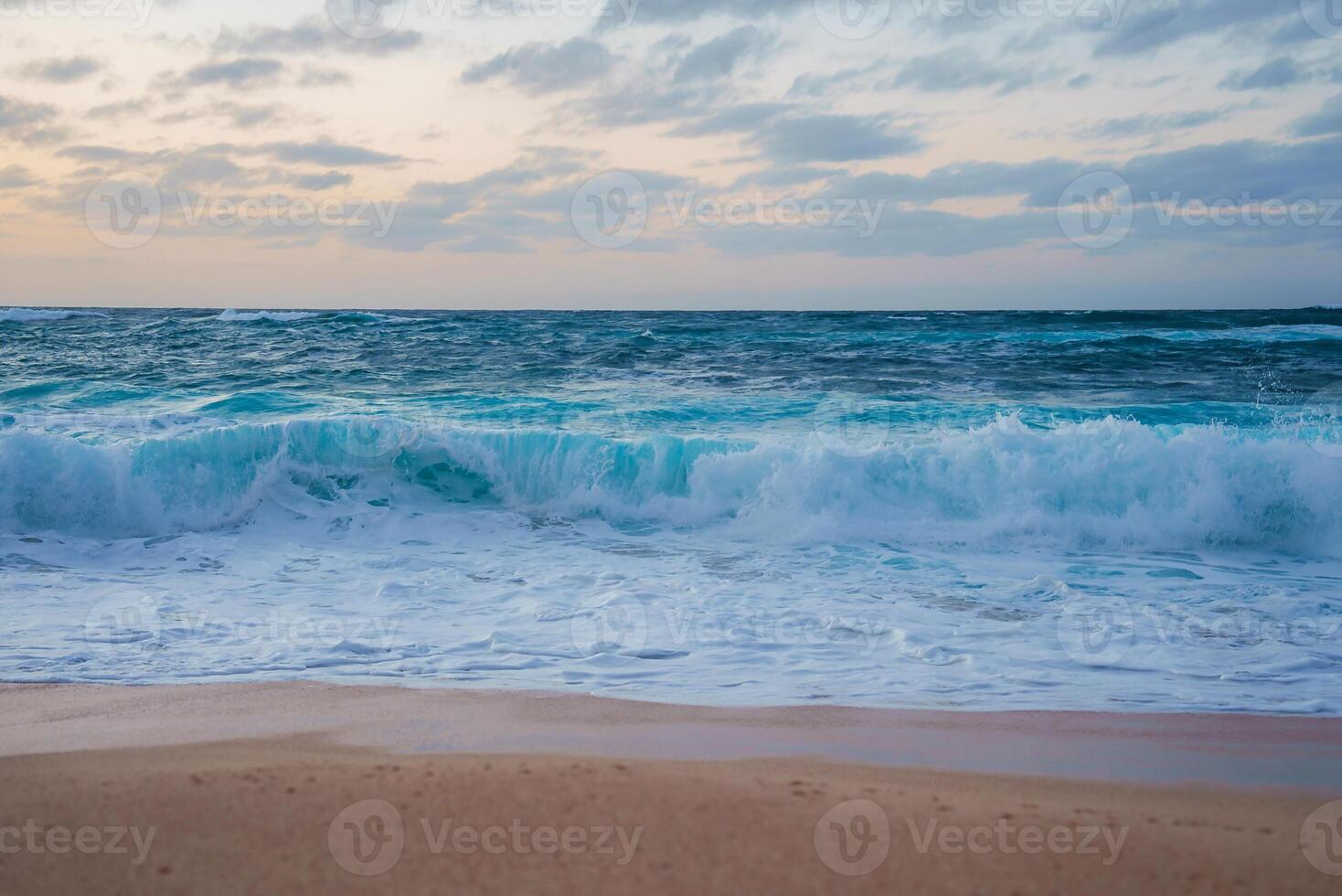 A tranquil beach scene with turquoise ocean waves, white foam, and a pastel colored sky. Soft light and clouds suggest a tropical coastal setting. photo