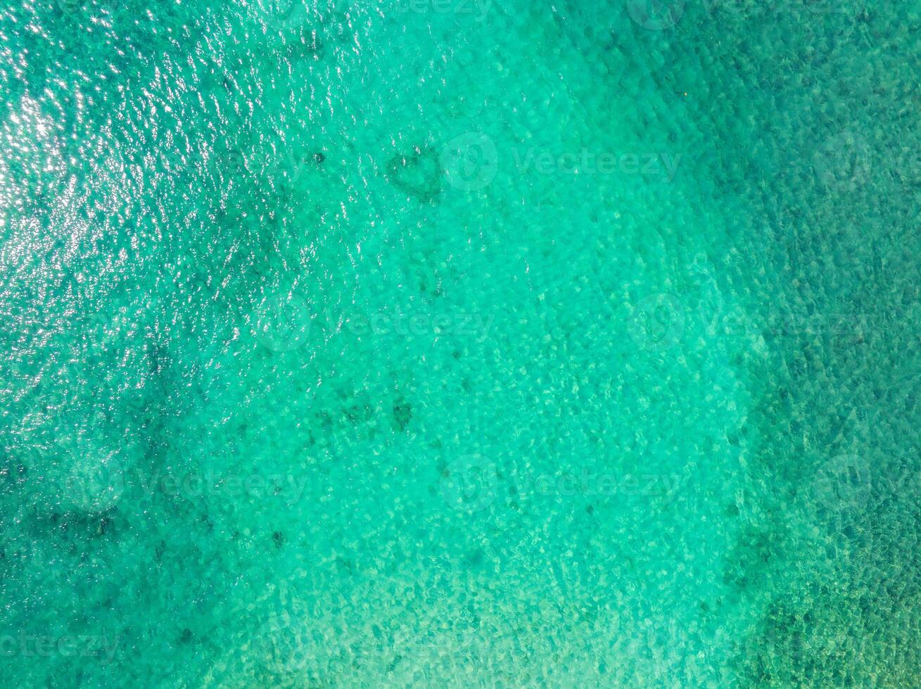 Aerial perspective of clear turquoise waters near Kauai island, Hawaii, with shimmering sunlight and visible underwater features like coral patches. photo
