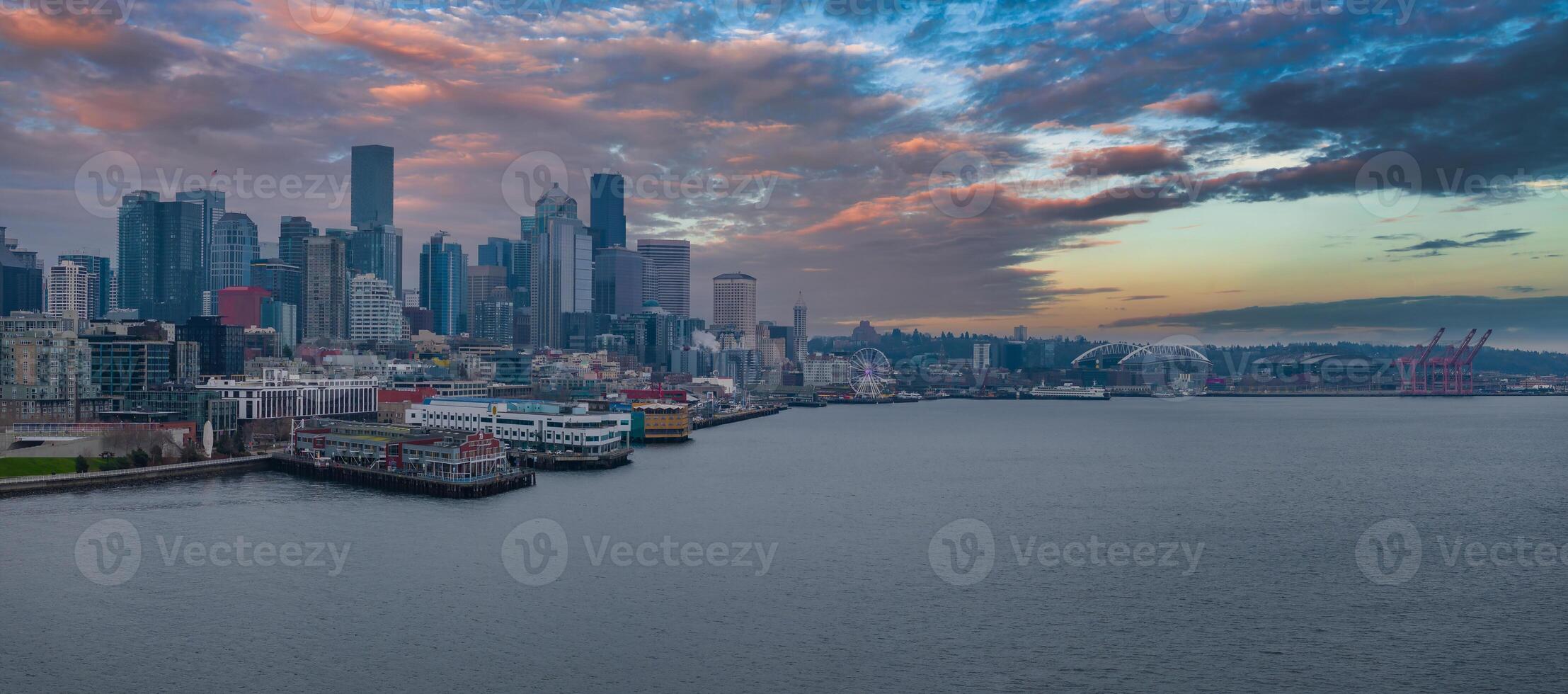 Downtown Seattle skyline with skyscrapers, the Seattle Great Wheel, T Mobile Park, Lumen Field, a cargo ship in the bay, and vibrant sunset clouds. photo