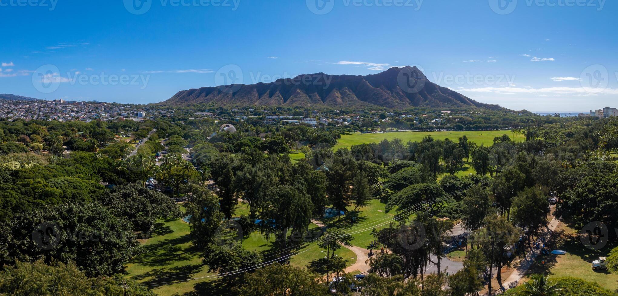 Aerial view of Diamond Head Crater on Oahu Island, Hawaii, with lush parkland, urban areas, and the ocean visible under a clear blue sky. photo