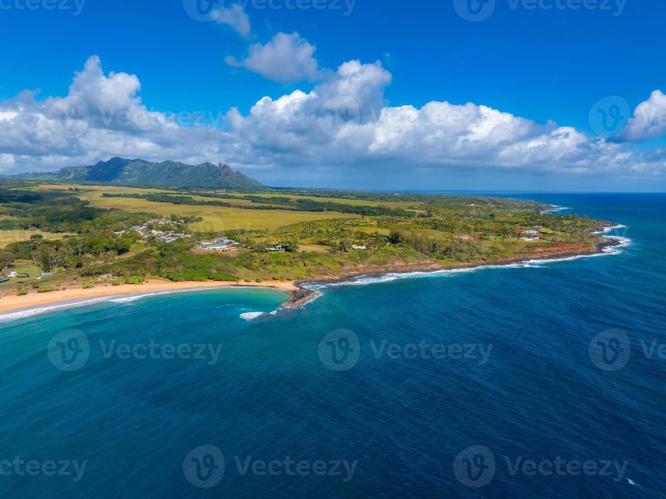 Aerial view of Kauai Island, Hawaii, showing golden beaches, turquoise waters, lush greenery, scattered buildings, and rugged mountains under a cloudy sky. photo