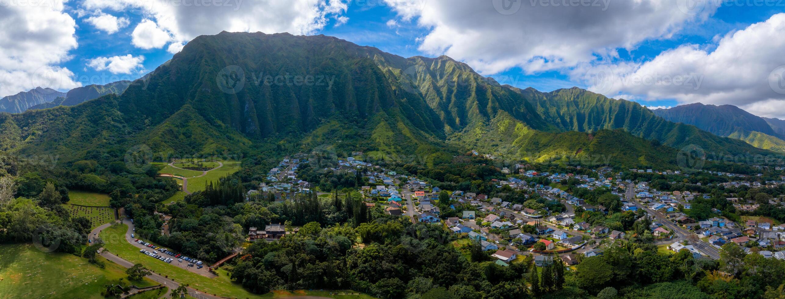 Aerial view of green mountains on Oahu island, Hawaii, with dense vegetation, a residential area, and a small temple like structure in the foreground. photo