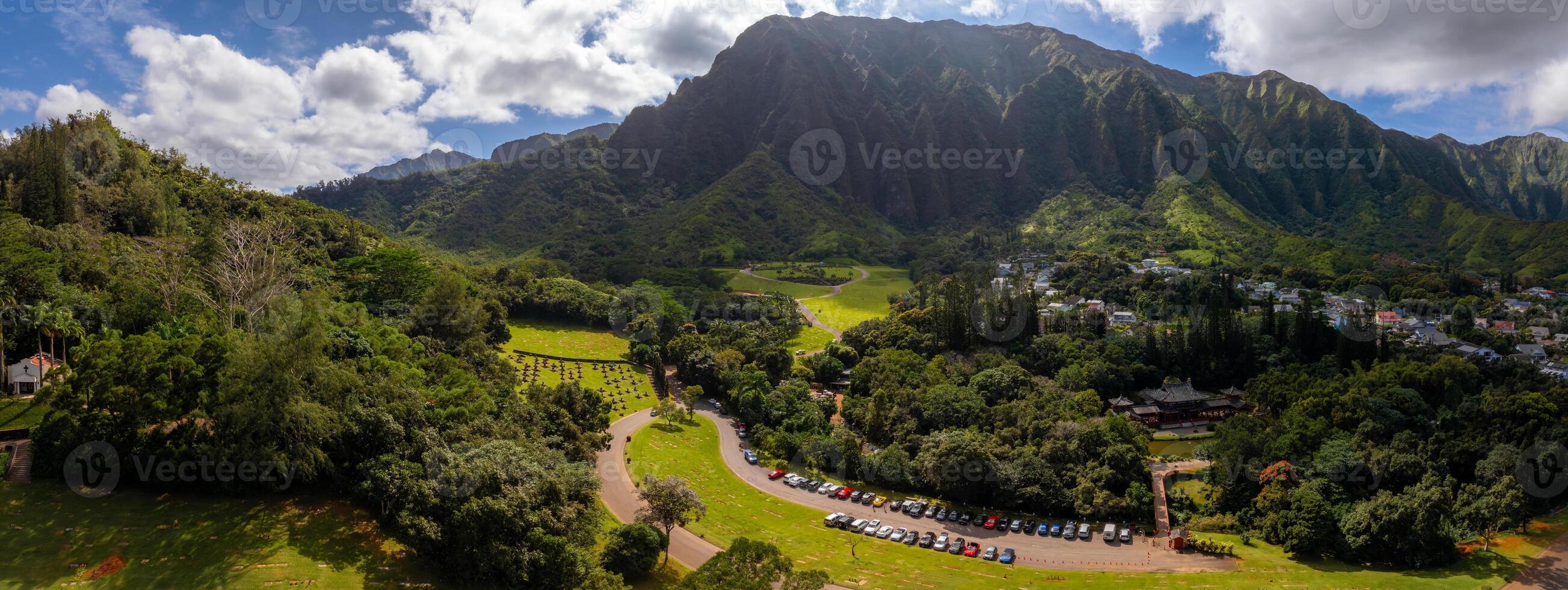 Aerial view of the Byodo In Temple surrounded by lush greenery, with the Ko olau mountain range in the background and a park in the foreground. photo