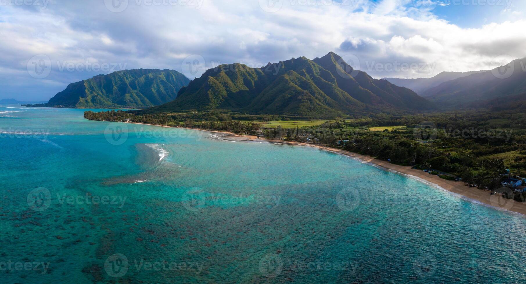 Aerial view of Oahu, Hawaii, showing turquoise waters, a sandy beach, and the lush Ko olau mountain range under a sky with scattered clouds. photo