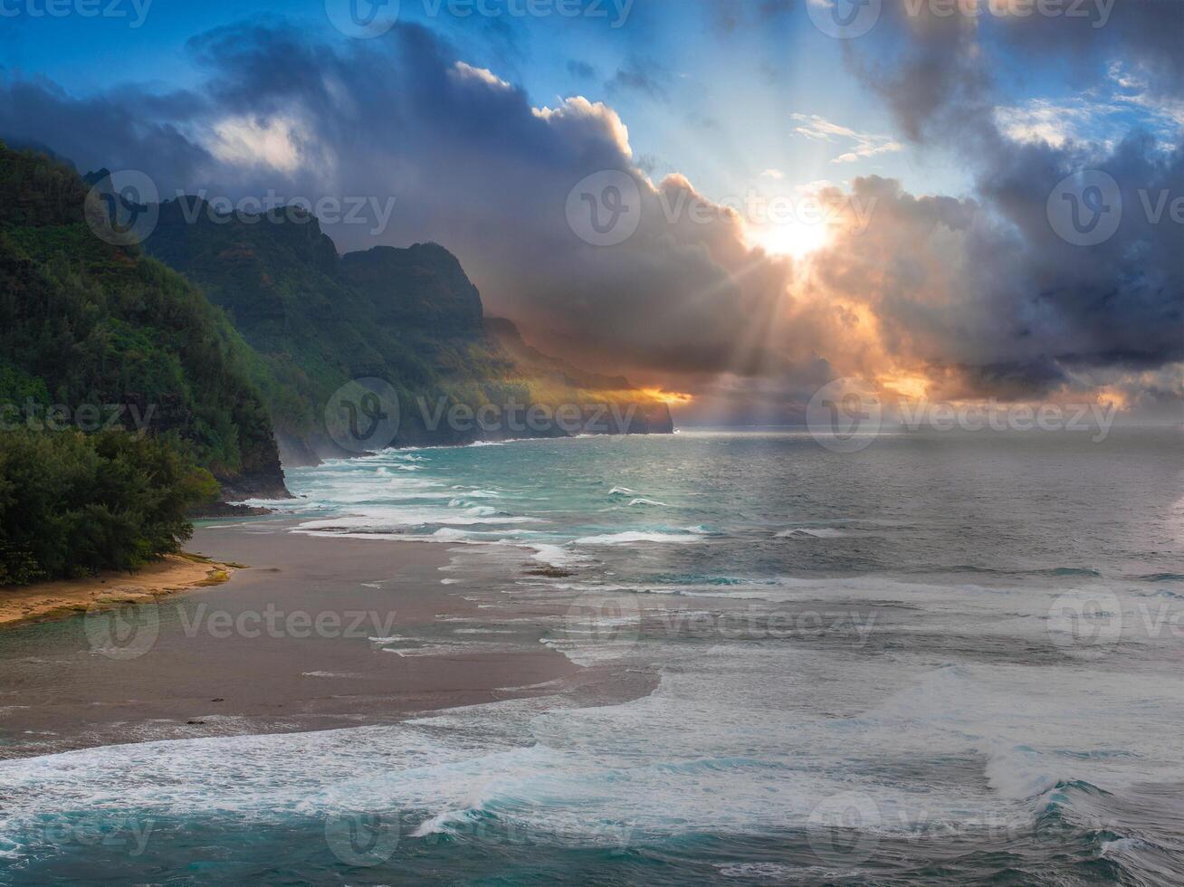 Aerial view of Kauai Island showing Napali Coast cliffs, lush greenery, sandy beach, turquoise waves, and sunlight breaking through clouds. photo