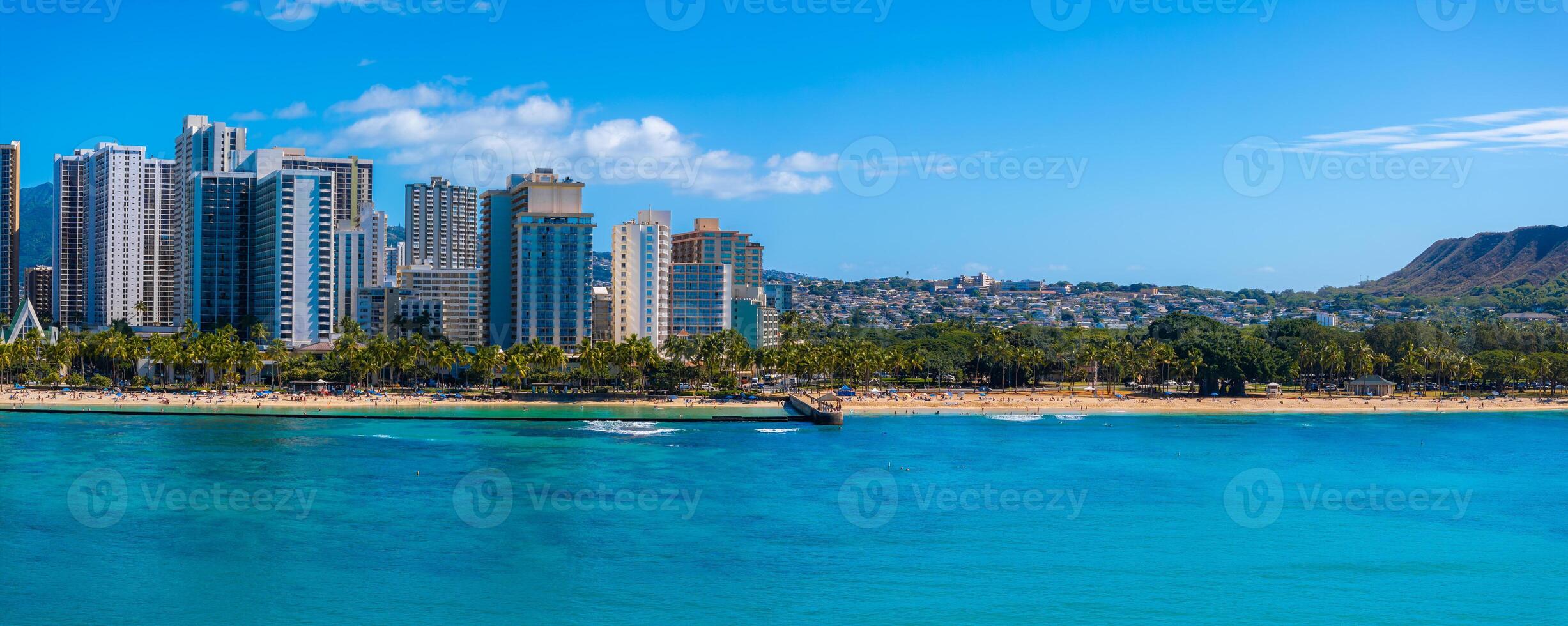 Turquoise waters, sandy beach with palm trees, modern skyline, and Diamond Head crater under a clear blue sky in Honolulu, Oahu, Hawaii. photo