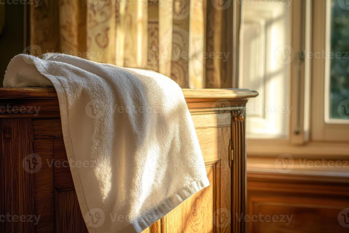 Cozy sunlit interior with white towel draped on wooden furniture by window photo