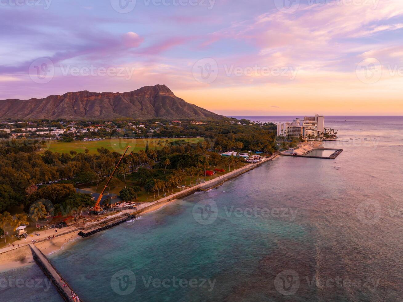 Aerial view of Waikiki Beach in Oahu, Hawaii, at sunset with Diamond Head Crater in the background, turquoise waters, sandy shore, and urban structures. photo