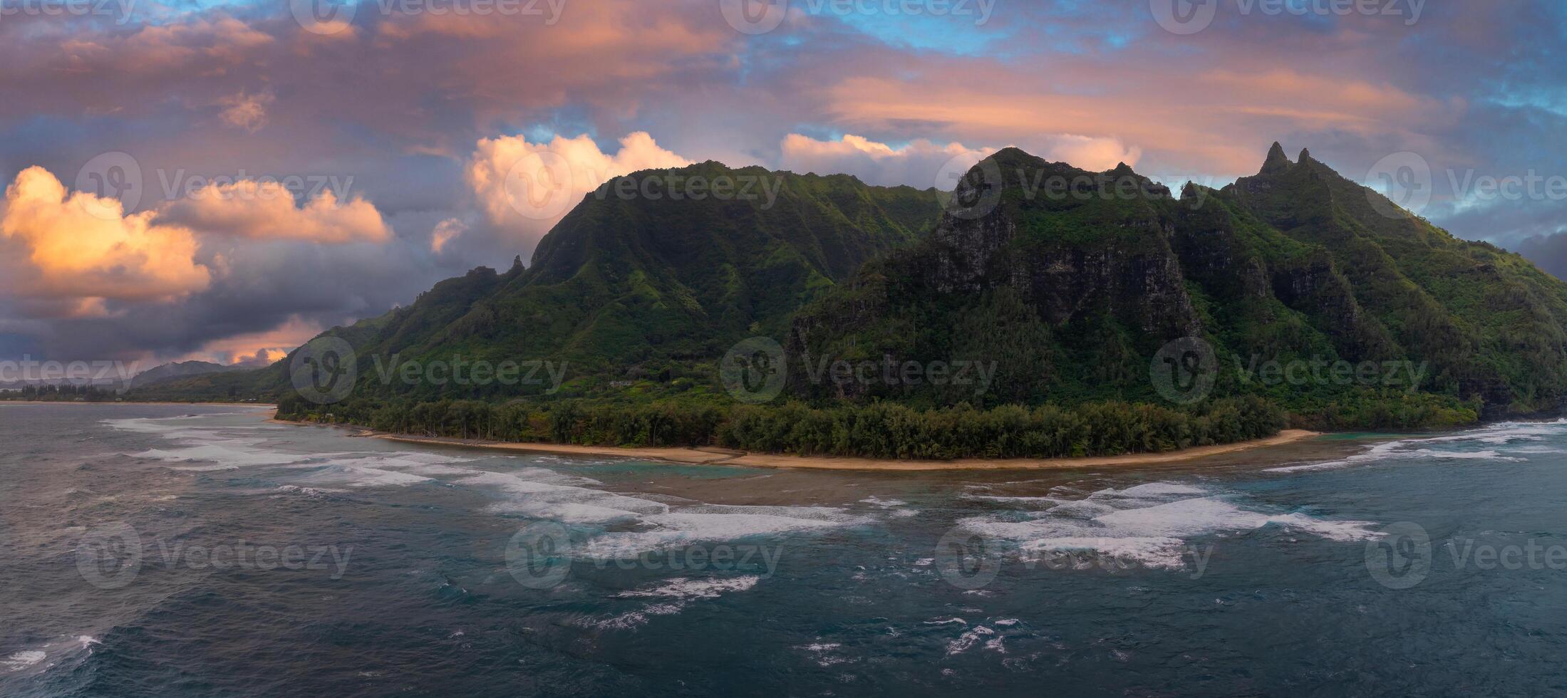 Aerial view of Kauai's Napali Coast with jagged green cliffs, sandy beach, turquoise waters, and a vibrant sunset blending orange and pink hues. photo