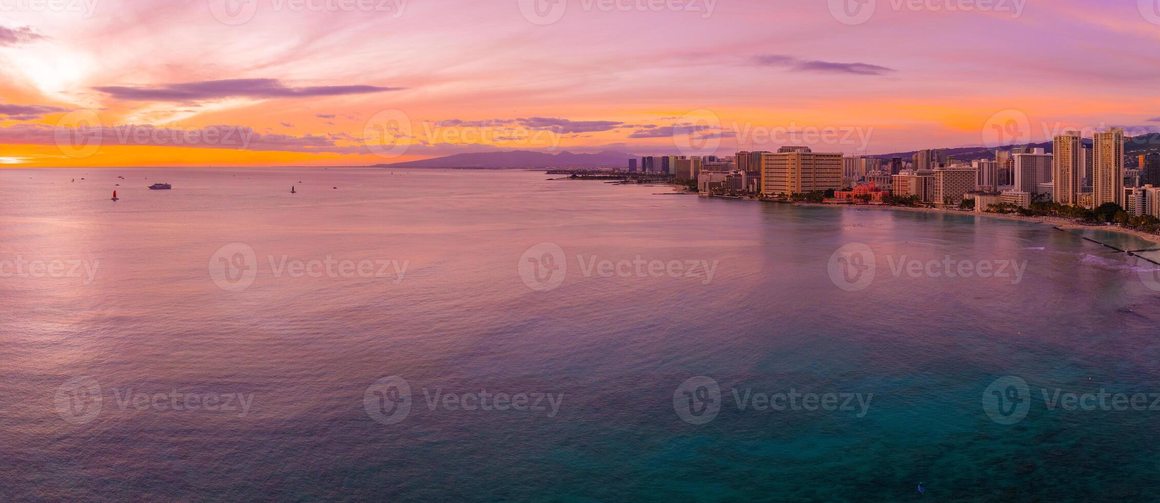 Aerial view of Waikiki Beach in Honolulu, Oahu, Hawaii, at sunset with high rise buildings, calm ocean, and Diamond Head Crater in the distance. photo
