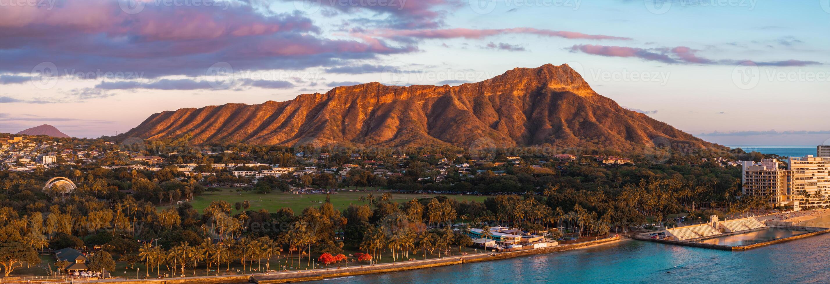 Aerial view of Diamond Head Crater on Oahu Island, Hawaii, at sunset. Golden light highlights the crater, park, palm trees, and turquoise shoreline. photo