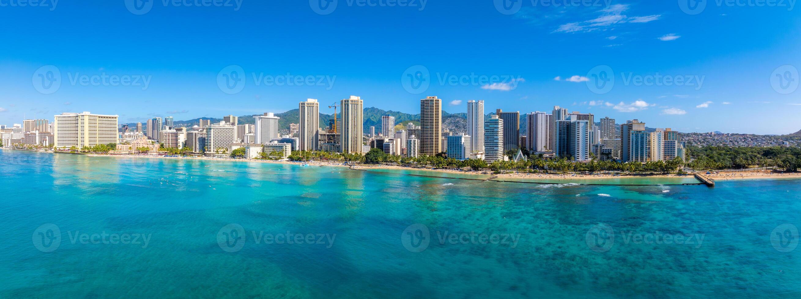Aerial view of Waikiki Beach in Honolulu, Hawaii, with turquoise waters, high rise buildings, lush greenery, and Diamond Head crater in the background. photo