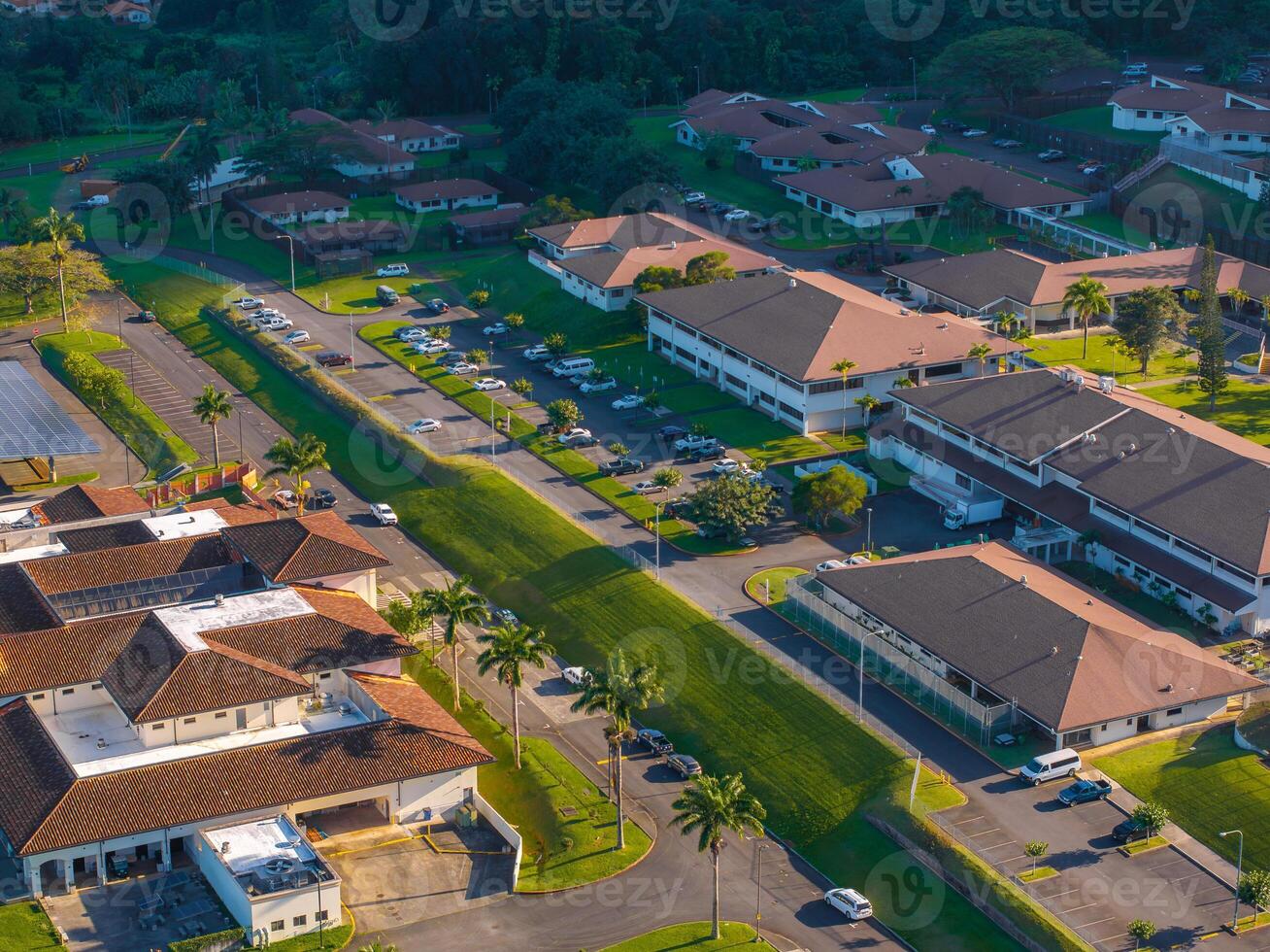 Neatly arranged buildings with red tiled roofs, central road, green spaces, and tropical vegetation on Oahu Island, Hawaii, seen from above. photo