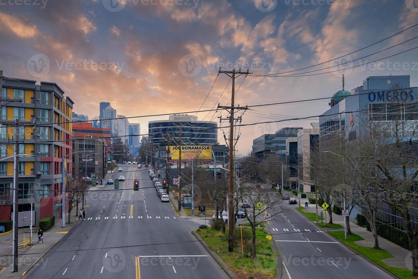 Street view in Seattle, USA, featuring downtown skyscrapers, a colorful sunset sky, modern buildings, and a Joe Bonamassa billboard. photo
