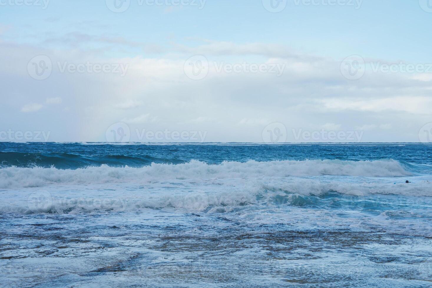 Waves Crashing on a Rocky Shoreline Under a Partly Cloudy Sky photo