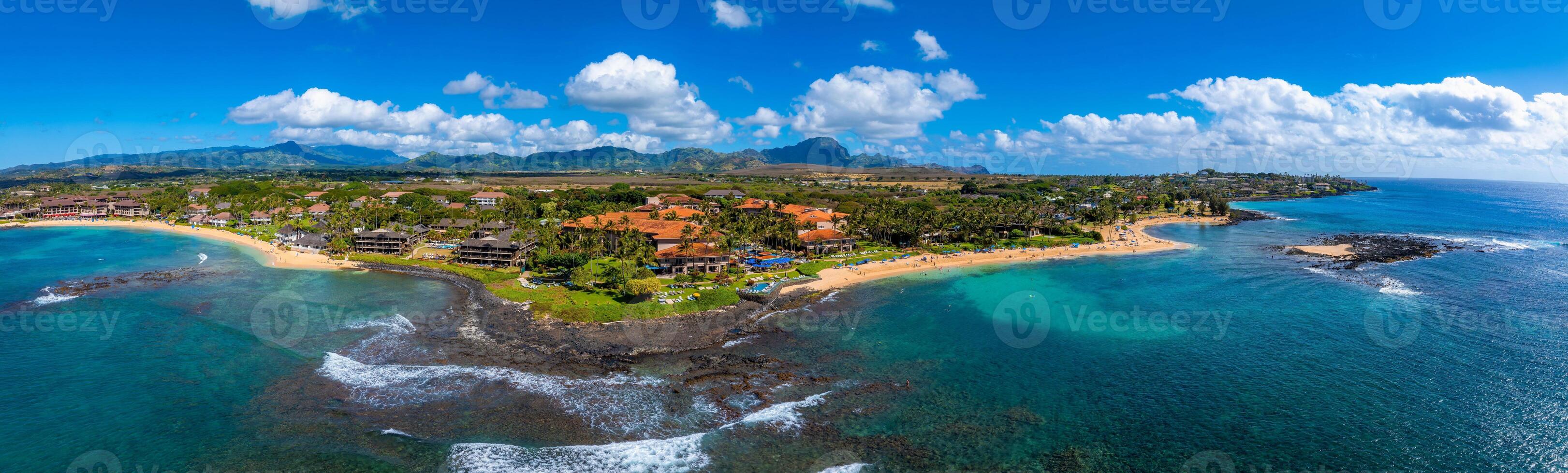 Aerial view of Kauai, Hawaii, showing golden beaches, turquoise waters, rocky outcrops, resorts with red tiled roofs, and the Napali cliffs in the background. photo