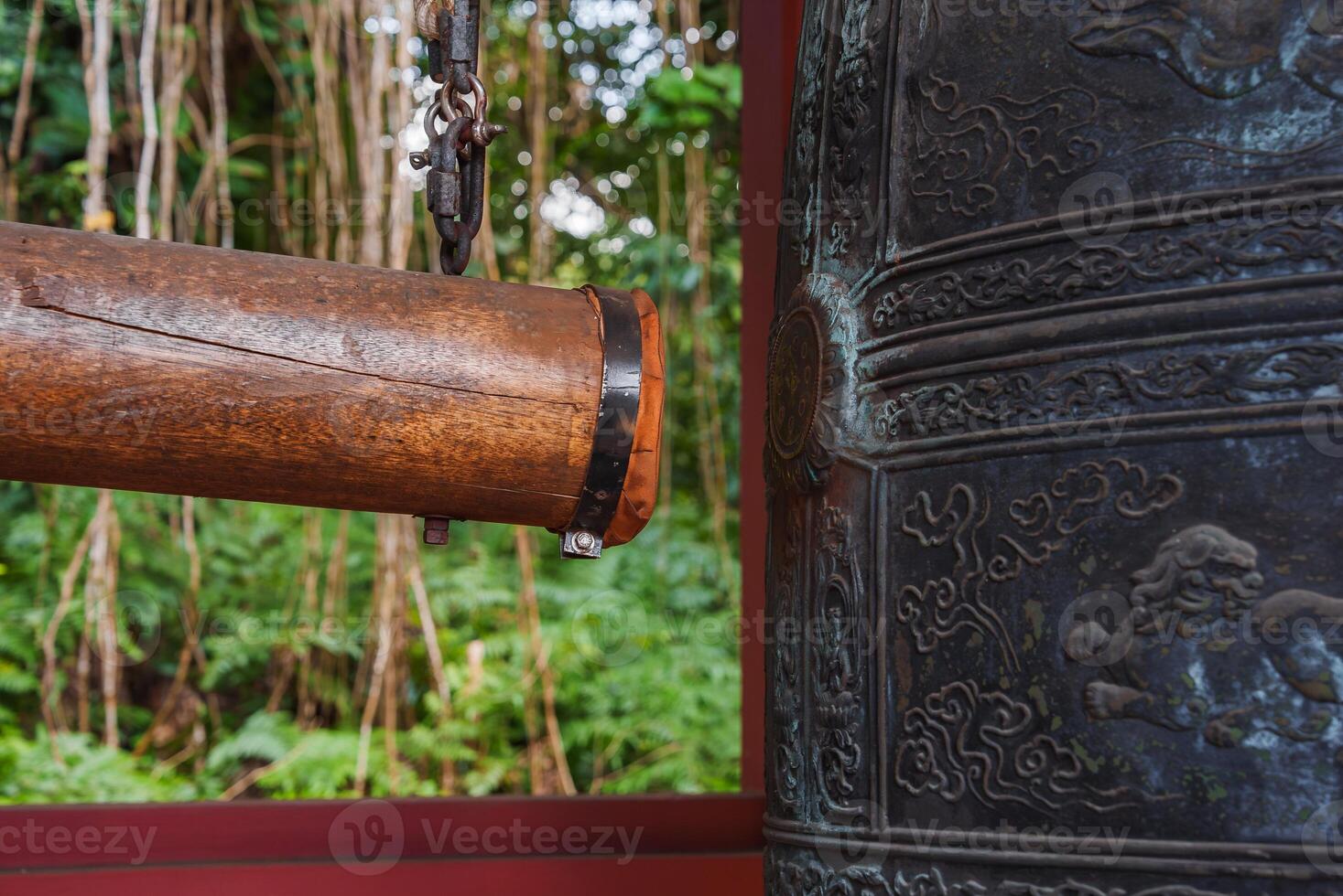 Traditional Japanese style bronze bell with intricate carvings and a wooden striker, set against lush green foliage at Byodo In Temple in Hawaii. photo