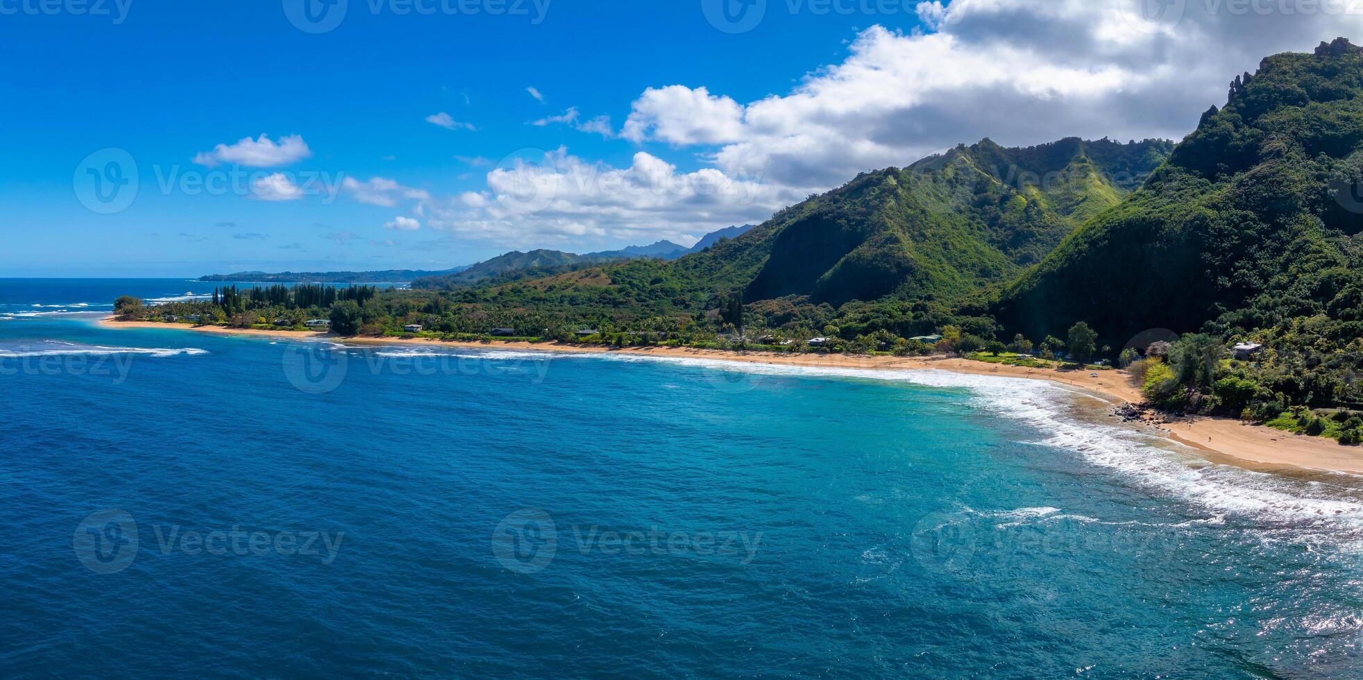 Aerial view of Kauai island's coastline, featuring turquoise waters, a sandy beach, lush Napali cliffs, and a bright sky with scattered clouds. photo