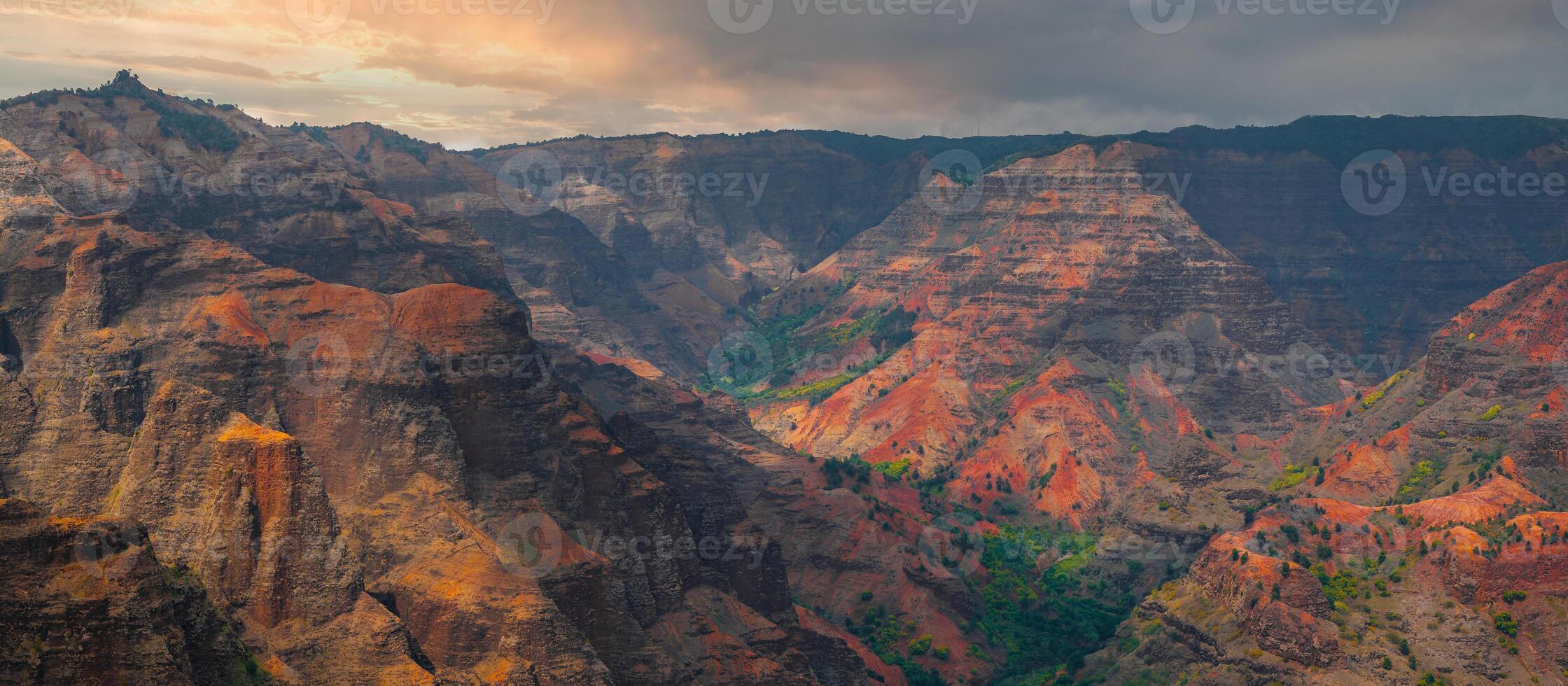 Waimea Canyon on Kauai Island, Hawaii, features vibrant red, orange, and green cliffs, deep valleys, and contrasting patches of lush vegetation. photo