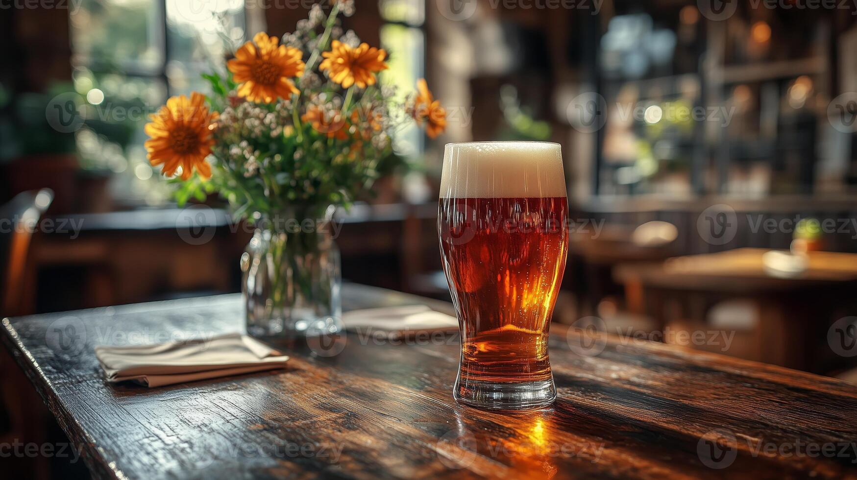 A beer glass sits on a table in front of a flower vase photo