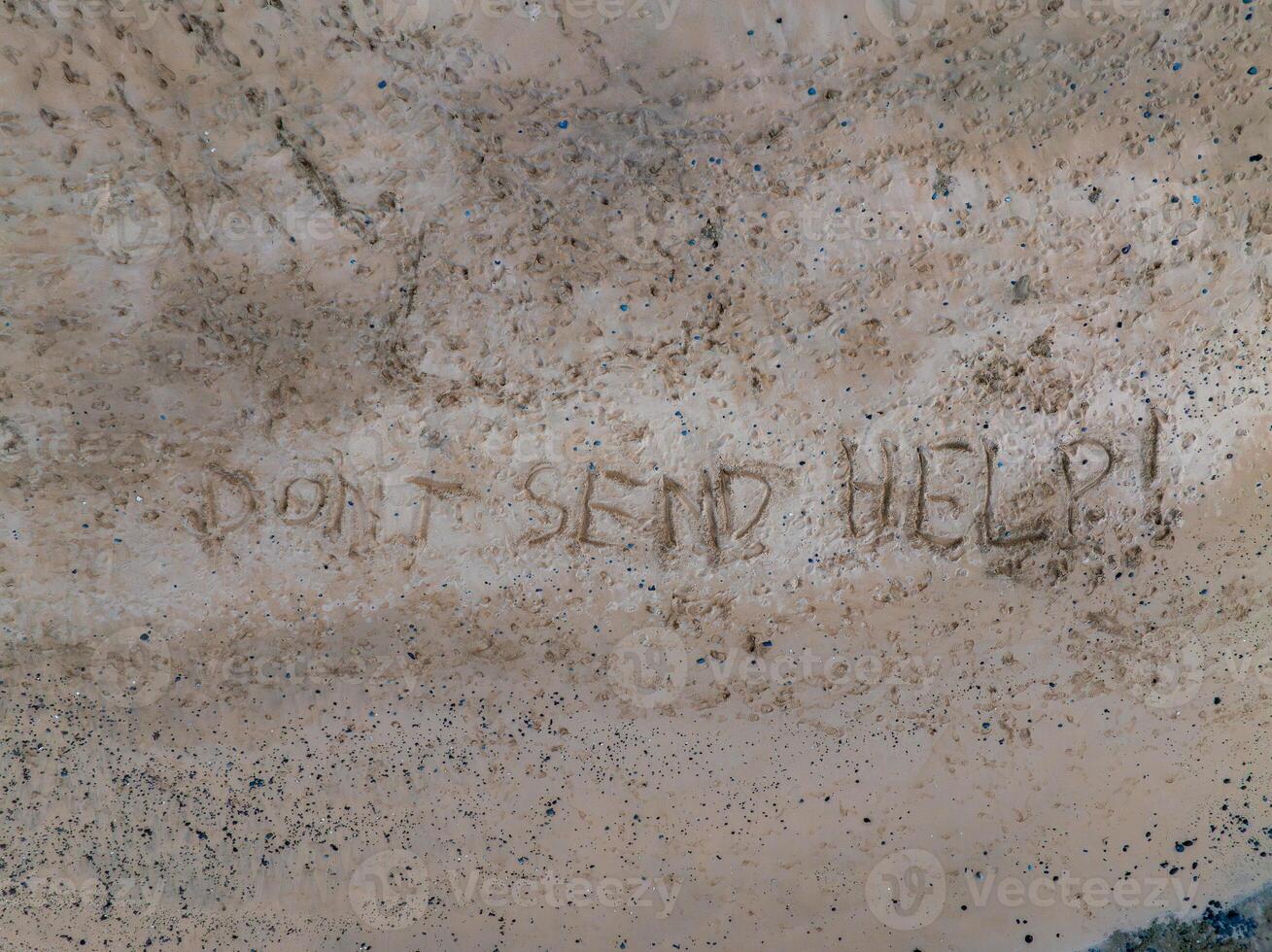 A sandy area features the message 'DON'T SEND HELP ' etched prominently, surrounded by scattered pebbles and debris, suggesting a coastal setting. photo