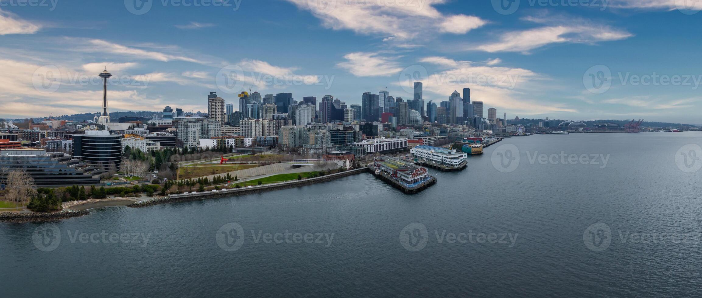 Downtown Seattle's skyline with the Space Needle, modern buildings, waterfront docks, a cargo ship in the bay, and a green park in the foreground. photo