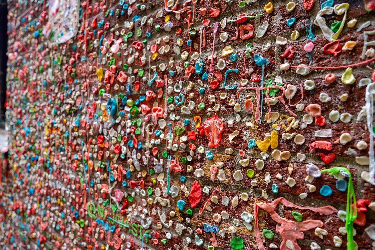 The Gum Wall in Seattle's Pike Place Market area features a brick wall covered in vibrant layers of chewed gum, creating a textured and colorful display. photo