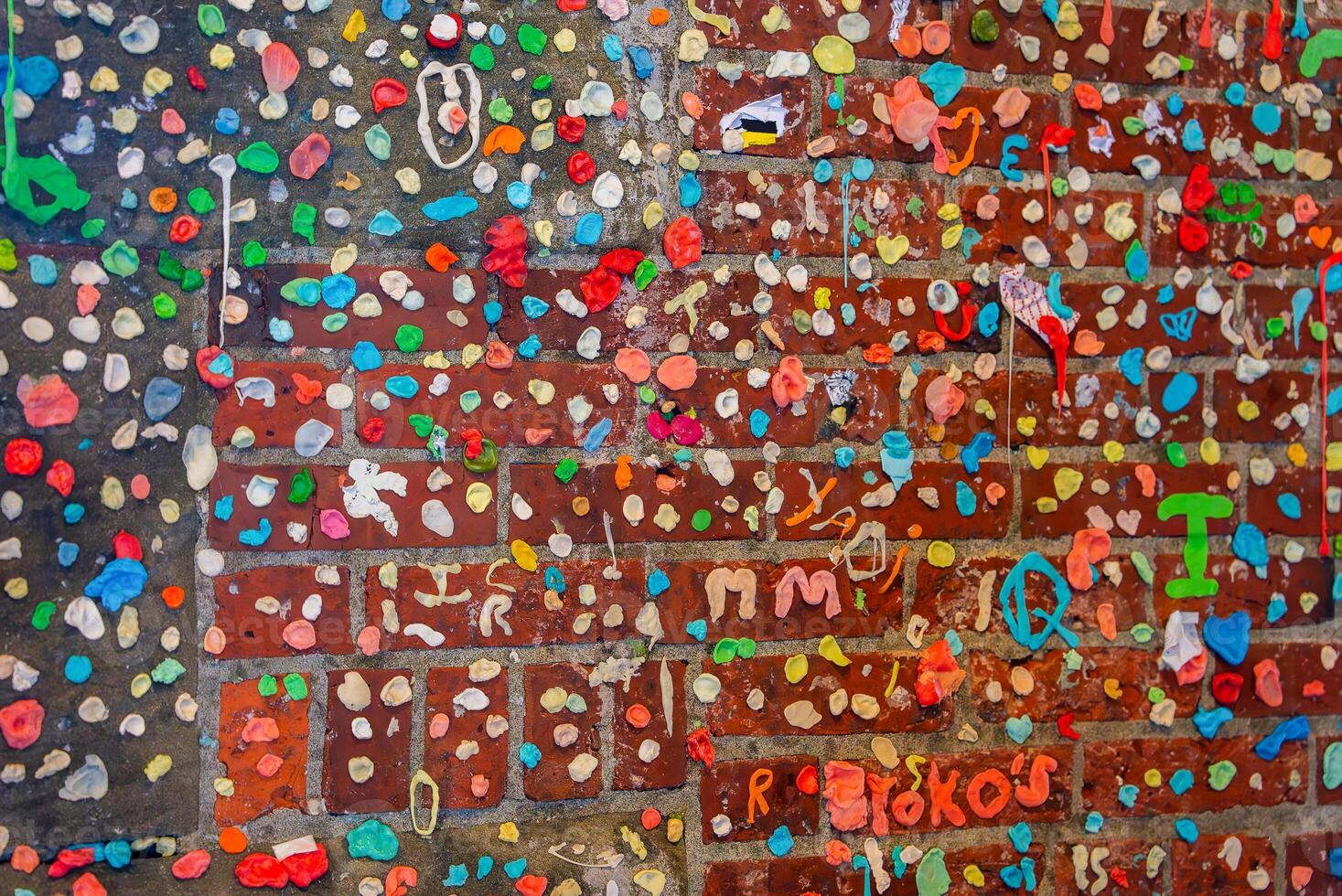 The Gum Wall in Seattle features a brick wall covered with chewed gum in vibrant colors, forming letters, symbols, and designs in Post Alley. photo